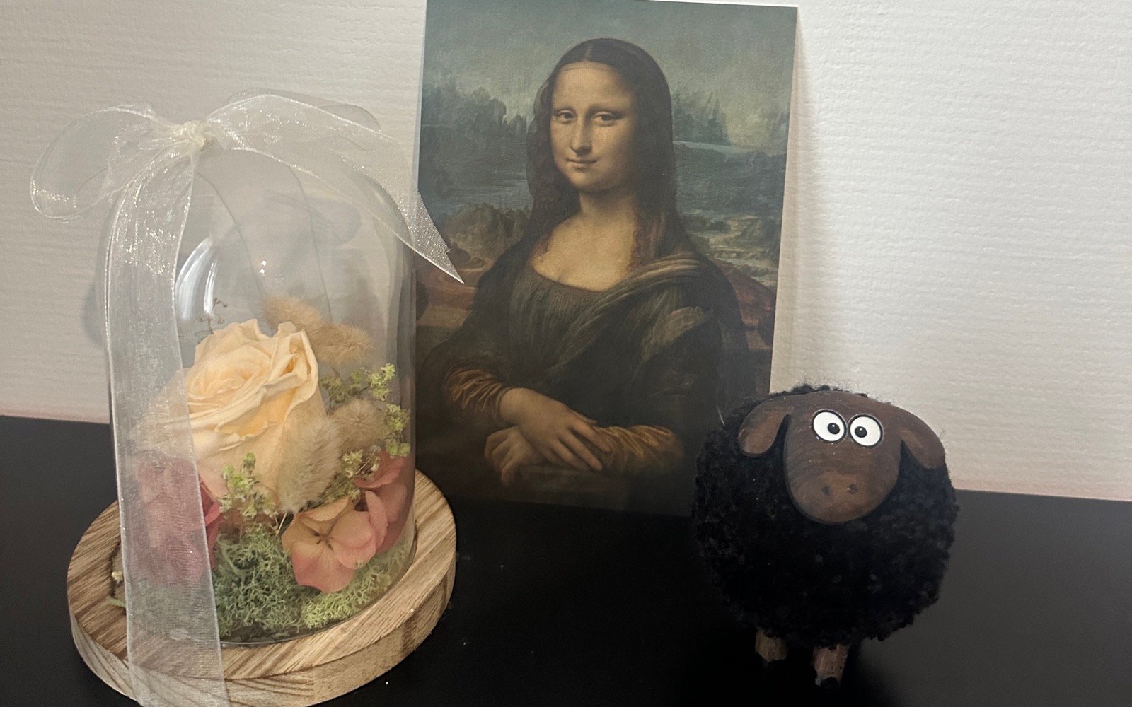 Preserved flowers, a Mona Lisa postcard, and a handmade sheep decoration on a desk.